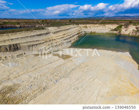 Large industrial site shows steep sandy cliffs and green water pool near flat land, under bright blue sky with some clouds during day Large industrial site shows steep sandy cliffs and green water pool near flat land, under bright blue sky with some clouds during day 139046550