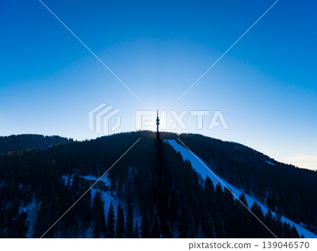 Snow-covered mountain with a tower standing tall against a bright blue sky during sunset hours in a winter landscape 139046570