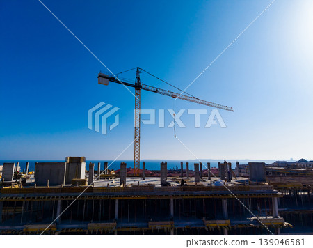 Construction site with crane working under clear blue sky near the ocean in midday light showing building progress and development activity Construction site with crane working under clear blue sky near the ocean in midday light showing building progress and development activity 139046581