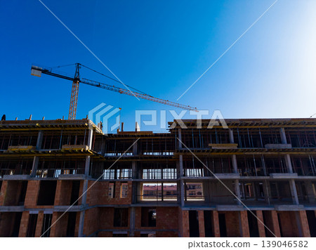 Construction of a multi-story building with a crane under a clear blue sky in an urban area during the day Construction of a multi-story building with a crane under a clear blue sky in an urban area during the day 139046582