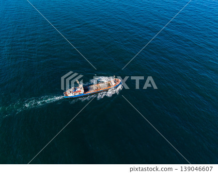 View of a cargo ship sailing over the wide blue ocean during daytime while leaving a wake of white foam behind in the clear waters 139046607