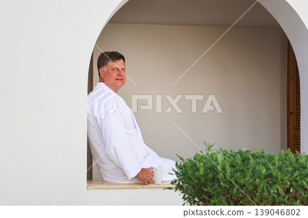 A man on vacation sits in a robe and drinks coffee A man on vacation sits in a robe and drinks coffee 139046802