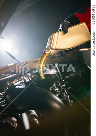Mechanic pouring engine oil into car engine in workshop. Automotive maintenance, oil change service and professional repair concept with dramatic lighting. 139046912