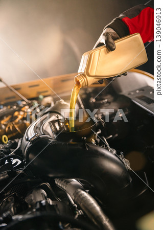 Mechanic pouring engine oil into car engine in workshop. Automotive maintenance, oil change service and professional repair concept with dramatic lighting. 139046913