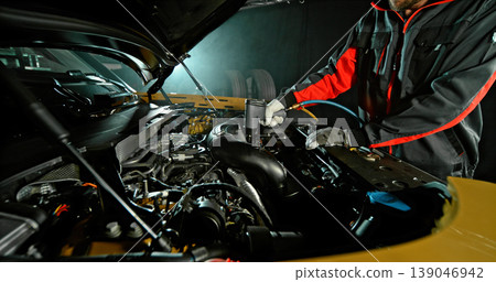 Mechanic repairing car engine in workshop, using tools with dramatic lighting. Automotive maintenance and professional service concept. Mechanic repairing car engine in workshop, using tools with dramatic lighting. Automotive maintenance and professional service concept. 139046942