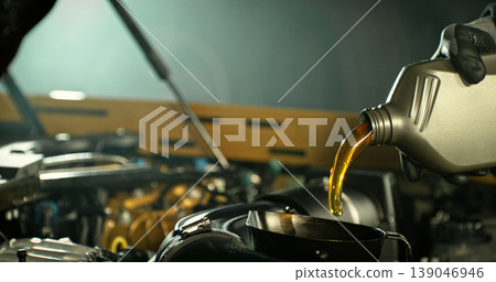 Mechanic pouring engine oil into car engine in workshop. Automotive maintenance, oil change service and professional repair concept with dramatic lighting. Mechanic pouring engine oil into car engine in workshop. Automotive maintenance, oil change service and professional repair concept with dramatic lighting. 139046946