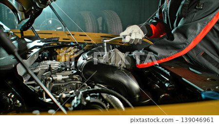 Mechanic repairing car engine in workshop, using tools with dramatic lighting. Automotive maintenance and professional service concept. Mechanic repairing car engine in workshop, using tools with dramatic lighting. Automotive maintenance and professional service concept. 139046961