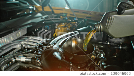 Mechanic pouring engine oil into car engine in workshop. Automotive maintenance, oil change service and professional repair concept with dramatic lighting. Mechanic pouring engine oil into car engine in workshop. Automotive maintenance, oil change service and professional repair concept with dramatic lighting. 139046963