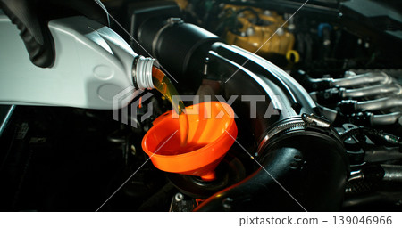 Mechanic pouring engine oil into car engine in workshop. Automotive maintenance, oil change service and professional repair concept with dramatic lighting. 139046966