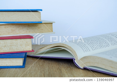 Open purple covered book leaning against stacked books on wooden tabletop representing reading, imagination, and quiet study moments. Open purple covered book leaning against stacked books on wooden tabletop representing reading, imagination, and quiet study moments. 139046997