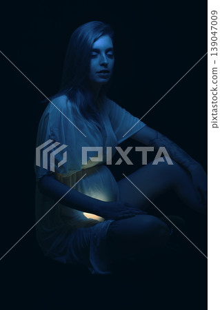 Sad young pregnant woman illuminated by blue fluorescent light Sad young pregnant woman illuminated by blue fluorescent light 139047009