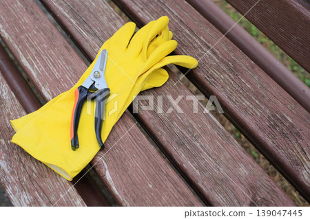 Yellow rubber gardening gloves and sharp pruning shears for pruning bushes, top view. Professional gardening tools for spring plant care Yellow rubber gardening gloves and sharp pruning shears for pruning bushes, top view. Professional gardening tools for spring plant care 139047445
