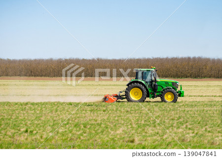Green tractor driving through agricultural field Green tractor driving through agricultural field 139047841