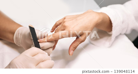 Manicurist filing woman's nails at her working table. Nail care process, close-up 139048114