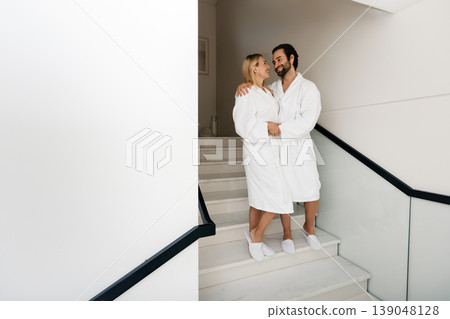 Beautiful couple wearing white bathrobes enjoying spa weekend while honeymoon walking at wellness center Beautiful couple wearing white bathrobes enjoying spa weekend while honeymoon walking at wellness center 139048128
