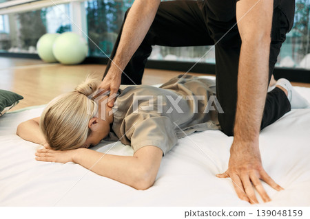 Female patient lying gymnastic mat receiving Yumeiho Japanese back and neck massage with alternative treatment specialist. Therapeutic massage Yumeiho Female patient lying gymnastic mat receiving Yumeiho Japanese back and neck massage with alternative treatment specialist. Therapeutic massage Yumeiho 139048159