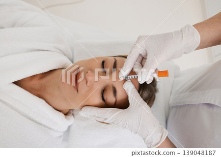 Pretty female while facial mesotherapy for wrinkles removal, top view. Beauty injections in woman's forehead for blocking mimic wrinkles Pretty female while facial mesotherapy for wrinkles removal, top view. Beauty injections in woman's forehead for blocking mimic wrinkles 139048187
