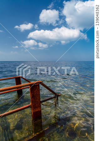 The remains of an old rusty bridge rust in the seawater, a clean, calm sea, and a concept for environmental awareness and a poster for Earth Day and Ecology The remains of an old rusty bridge rust in the seawater, a clean, calm sea, and a concept for environmental awareness and a poster for Earth Day and Ecology 139048362