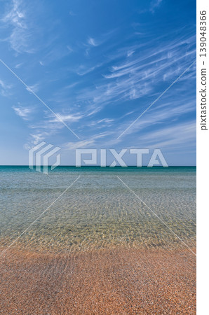 Calm ocean meets pebbled shore under vast blue sky with light clouds 139048366