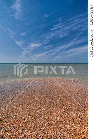 shell beach and a calm, clear sea, copy space. A concept for advertising a vacation on the magnificent beaches of the Mediterranean, a sky with wispy clouds shell beach and a calm, clear sea, copy space. A concept for advertising a vacation on the magnificent beaches of the Mediterranean, a sky with wispy clouds 139048367