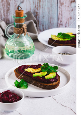 Beetroot hummus and avocado on rye bread on a plate on the table vertical view Beetroot hummus and avocado on rye bread on a plate on the table vertical view 139048762