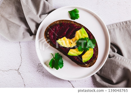 Close up of beetroot hummus and avocado on rye bread on a plate on the table top view Close up of beetroot hummus and avocado on rye bread on a plate on the table top view 139048765