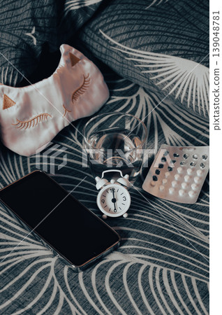 Insomnia medication, water, a smartphone, and a mask on the bed vertical view 139048781