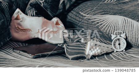Sleeping pills, a glass of water, a mask, and an alarm clock on the bed web banner Sleeping pills, a glass of water, a mask, and an alarm clock on the bed web banner 139048785