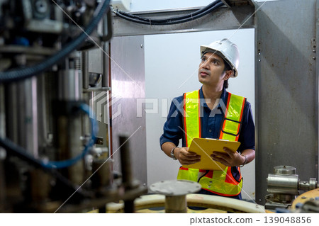 Asian factory technician or engineer hold document file and stand in front of containing machine to check the quality of the line product and function of machine with standard control for good Asian factory technician or engineer hold document file and stand in front of containing machine to check the quality of the line product and function of machine with standard control for good 139048856