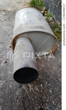 Muffler resting on the ground shows signs of wear and rust on a concrete surface Muffler resting on the ground shows signs of wear and rust on a concrete surface 139049017