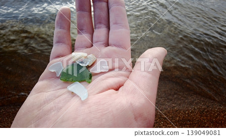 Hand holding pieces of sea glass on a beach near water on a sunny day Hand holding pieces of sea glass on a beach near water on a sunny day 139049081