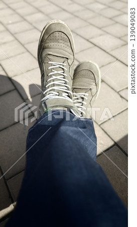 Person sits with legs crossed and shoes on pavement in a sunny setting 139049083