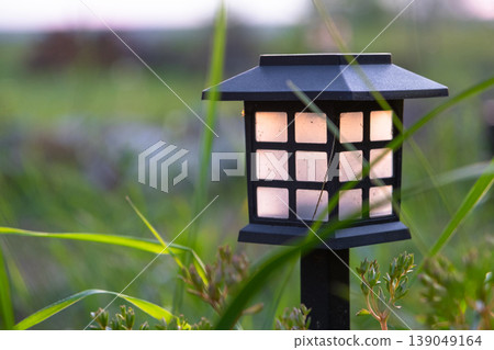Decorative solar lantern in flowerbed, landscape LED garden light, perennial border of daylilies, grasses, mulch, boulders, modern natural style. Decorative solar lantern in flowerbed, landscape LED garden light, perennial border of daylilies, grasses, mulch, boulders, modern natural style. 139049164