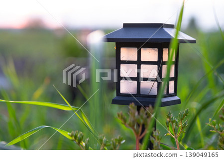 Solar powered landscape lantern, decorative flowerbed with daylilies, ornamental grasses, natural mulch, eco garden, contemporary minimalism. Solar powered landscape lantern, decorative flowerbed with daylilies, ornamental grasses, natural mulch, eco garden, contemporary minimalism. 139049165