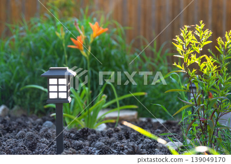 Solar landscape lantern, perennial garden border with daylilies, grasses, mulch and large stones, eco night lighting, natural contemporary style. Solar landscape lantern, perennial garden border with daylilies, grasses, mulch and large stones, eco night lighting, natural contemporary style. 139049170
