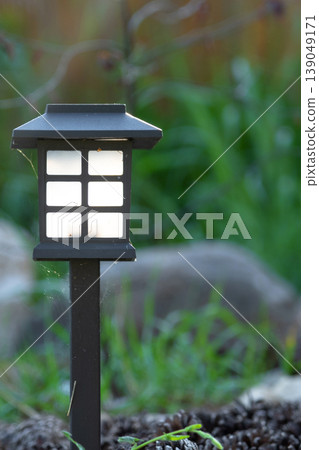 Minimalist solar lantern for flowerbed, perennial grasses, mulch and boulders, accent LED garden light, eco-friendly night landscape, modern style. Minimalist solar lantern for flowerbed, perennial grasses, mulch and boulders, accent LED garden light, eco-friendly night landscape, modern style. 139049171