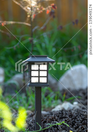 Perennial flowerbed with solar garden lamp, mulch, large boulders, mix of grass and lilies, minimalist eco design, night LED accent lighting. Perennial flowerbed with solar garden lamp, mulch, large boulders, mix of grass and lilies, minimalist eco design, night LED accent lighting. 139049174
