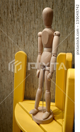 Wooden mannequin stands on yellow chair in studio or workspace during daytime 139049742