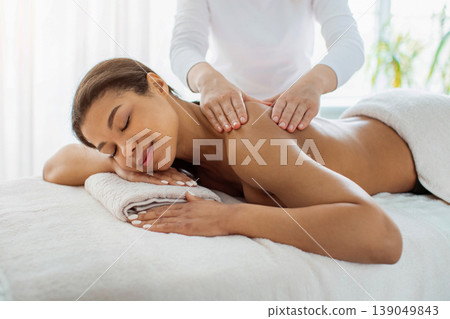 Young African American woman enjoying relaxing back massage at luxury spa salon 139049843