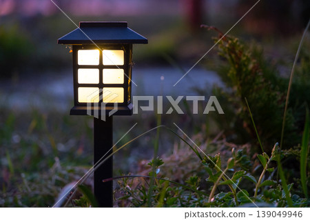 Decorative solar lantern, perennial border with grasses and mulch, LED accent light, modern and sustainable landscape garden style. Decorative solar lantern, perennial border with grasses and mulch, LED accent light, modern and sustainable landscape garden style. 139049946