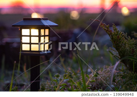 Japanese style solar landscape lantern, decorative flowerbed, ornamental grass, mulch, evening LED garden lighting, eco-friendly outdoor design. Japanese style solar landscape lantern, decorative flowerbed, ornamental grass, mulch, evening LED garden lighting, eco-friendly outdoor design. 139049948