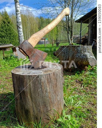 Close-up of an old hatchet in a tree stump in a rural countryside yard. Close-up of an old hatchet in a tree stump in a rural countryside yard. 139050083