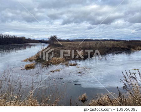 Thin ice crust on a river surface with dry yellow grass on the shore. 139050085