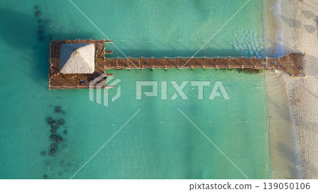 Drone shot of a small hut on a wooden pier on sandy beach with turquoise water 139050106