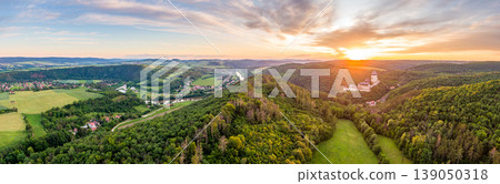 Aerial panorama view of Karsltejn castle with near village and forest, during the beautiful sunset. Small mountains and lake in background. Beautiful sky, dramatic clouds. Vibrant colors of nature. 139050318