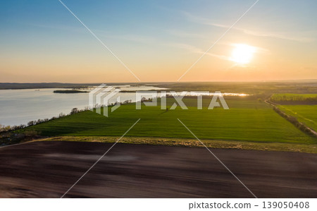 Aerial view of agriculture land at Palava hills, Czech republic. Rural scene near vineyards with power line above dirty road. Summer weather, sunset time. Nove mlyny water lake in background. Aerial view of agriculture land at Palava hills, Czech republic. Rural scene near vineyards with power line above dirty road. Summer weather, sunset time. Nove mlyny water lake in background. 139050408