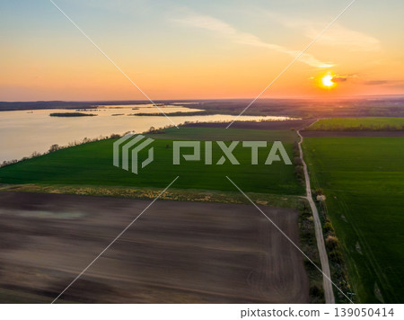 Aerial view of agriculture land at Palava hills, Czech republic. Rural scene near vineyards with power line above dirty road. Summer weather, sunset time. Nove mlyny water lake in background. Aerial view of agriculture land at Palava hills, Czech republic. Rural scene near vineyards with power line above dirty road. Summer weather, sunset time. Nove mlyny water lake in background. 139050414