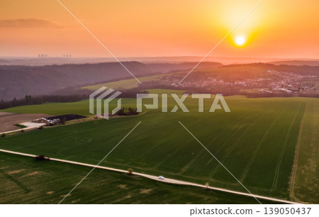 Aerial view of agriculture land during beautiful sunset. Fields and meadow with the small village in far. Vibrant soft colors at magic dusk. The asphalt road leading between fields with tree on side 139050437