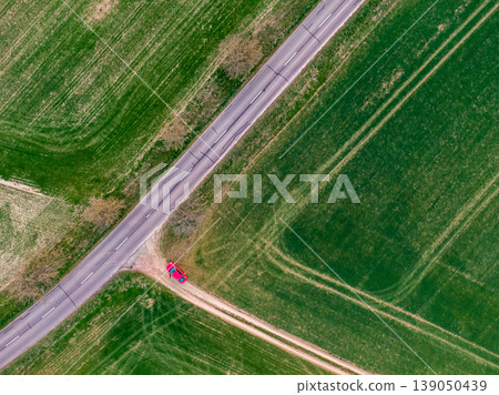 Red car is parking on the green field near the asphalt road. Aerial top down view, agriculture theme. Fresh green color at spring during the sunset. Rural scene on countryside Red car is parking on the green field near the asphalt road. Aerial top down view, agriculture theme. Fresh green color at spring during the sunset. Rural scene on countryside 139050439