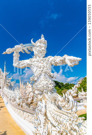 The white temple (Wat Rong Khun) in Chiang Rai city, Thailand. Beautiful buddhist ancient building with bridge above damned souls of sinners, path to the heaven. Famous tourist destination. Blue sky 139050555